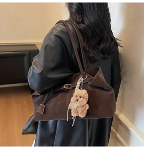 Detailansicht einer großen braunen Ledertasche mit Plüschbären-Anhänger an der Schulter