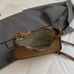 Bolso bandolera de ante marrón con cadena dorada y correa ajustable sobre una chaqueta