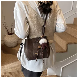 Detailansicht der dunkelbraunen Vintage Eimer-Tasche mit weißen Nähten und flauschigem Anhänger