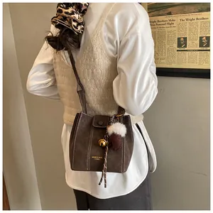 Detail der dunkelbraunen Beuteltasche mit Plüsch-Anhängern an einem stylischen Model