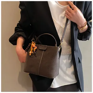 Détail d'un sac seau en cuir marron foncé avec breloque en bois et bandoulière