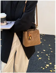 Détail du sac seau en daim marron avec pendentif en bois et fine bandoulière