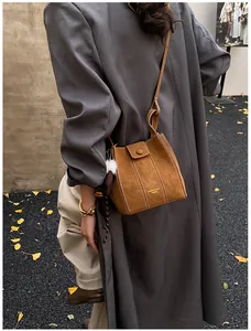 Detailansicht der braunen Wildleder-Beuteltasche mit Ziernaht und Plüsch-Anhänger im Herbst