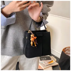 Détail du sac seau en cuir noir avec breloque en perles de bois et finitions dorées