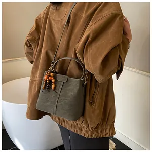 Détail d'un sac seau en cuir vert foncé avec breloque en perles sur un modèle féminin