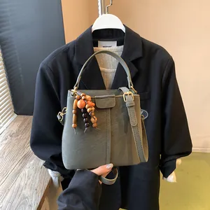 Sac seau vert olive en cuir texturé avec breloque en bois tenu par un mannequin