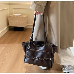 Detail of dark brown tote bag featuring decorative belt buckles and zip pockets