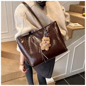 Détail du sac cabas en cuir brillant marron foncé avec un charmant ours en peluche pour femme