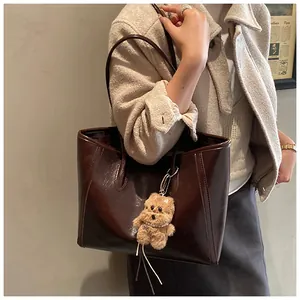 Détail d'un grand cabas en cuir marron brillant avec surpiqûres et charm ours en peluche