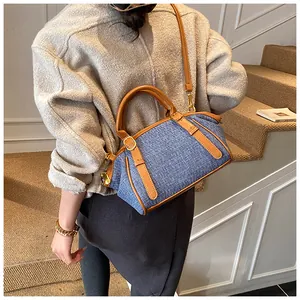 Detail of blue canvas crossbody bag with brown leather trim and metallic buckles