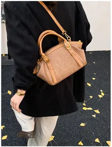 Close-up of brown woven crossbody bag styled with black coat on ginkgo leaves ground