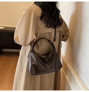 Détail d'un grand sac hobo en daim marron foncé avec bandoulière réglable et ferrures dorées