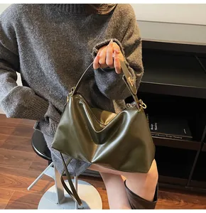 Détail d'un sac bandoulière en daim vert foncé avec fermoir rotatif et texture cuir souple