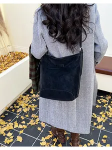 Detail of black suede hobo bag shown with a herringbone coat in autumn setting