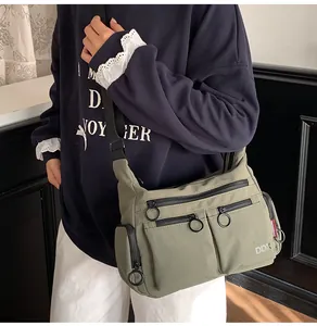Detail of multi-pocket green crossbody bag with black zippers and durable nylon strap