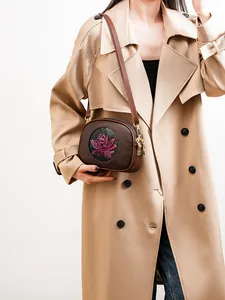 Brown leather crossbody bag with purple lotus embossing shown on a trench coat model