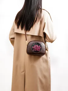 Detail of vintage brown crossbody bag featuring an embossed pink lotus pattern and gold hardware