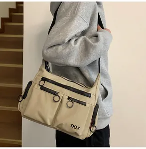 Detail of beige nylon crossbody bag with multiple zippers and large round ring pulls