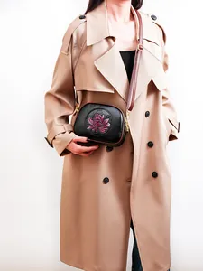 Detail of black Boston bag with pink lotus embossing worn with a beige trench coat