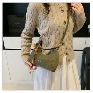 Detail of dark green matte crescent bag with wooden bead charm and plush pompom accessory