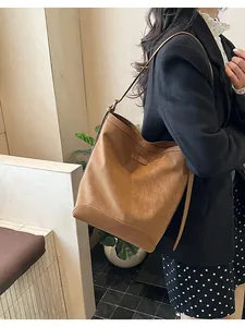 Detail of a large brown matte leather bucket bag worn by a model in a warm setting