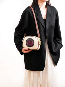 Detail of cream leather shoulder bag featuring a red lotus pattern and gold hardware accents