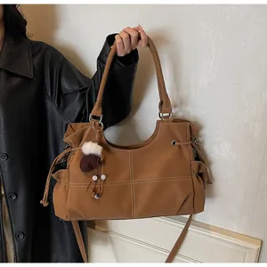 Detail of caramel brown tote bag with white cross-stitching and plush glove charm