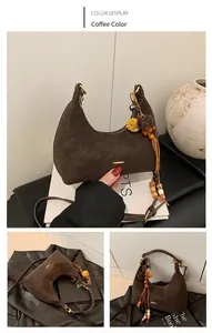 Detail view of coffee brown suede crescent bag with flower pendant and metal accents