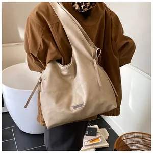 Detail view of the beige oil wax leather tote bag with rectangular metal plaque and ties
