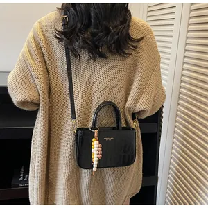 Detalle de bolso bandolera negro con relieve de cocodrilo y colgante de cuentas de colores