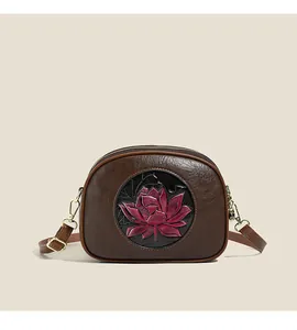 Close-up of brown textured leather crossbody bag featuring a pink lotus flower relief