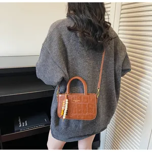 Bolso mini marrón con grabado de cocodrilo llevado como bandolera por una modelo en suéter