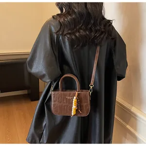 Detalle de bolso cuadrado marrón oscuro con textura de cocodrilo y colgante de cuentas