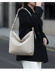 Detail of hobo bucket bag featuring a ruffled shoulder strap and soft beige leather finish