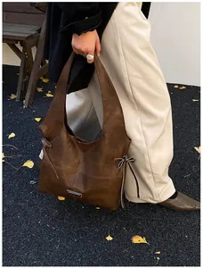 Detail view of large brown oil-wax leather tote with bow and metallic plaque accents