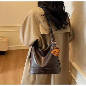 Detail of dark coffee vintage bucket bag with plush bear charm on trench coat