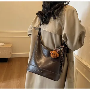Detail of dark brown vintage leather hobo bag with cute plush bear charm on beige coat