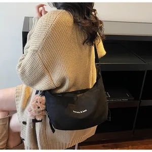 Détail d'un grand sac bandoulière noir en forme de croissant avec lettrage blanc et porte-clé