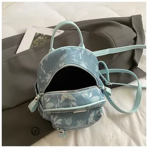 Mini floral canvas backpack with light blue leather straps on a dark grey blazer background