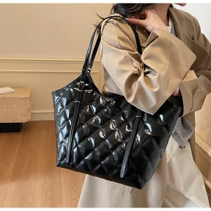 Close-up of black glossy quilted tote bag with adjustable strap on a stylish model
