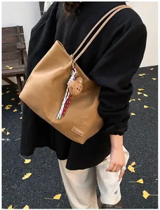 Detailed close-up of brown tote bag with bear charm and woven tassel on street background