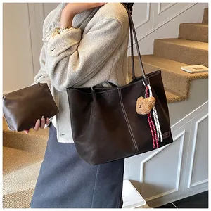 Detail of dark brown leather tote bag with white contrast stitching and bear charm