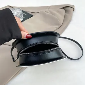 Minimalist black round crossbody bag showing internal capacity and zipper detail