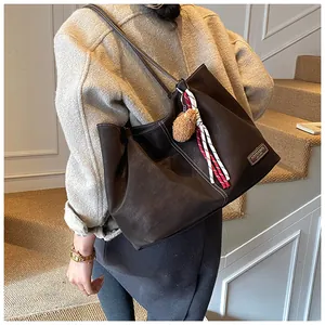 Detail view of dark brown leather tote bag featuring a decorative tassel and logo plaque