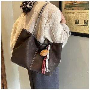 Detail of dark brown tote bag with contrast stitching and teddy bear charm on shoulder