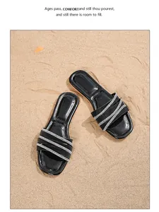 Details schwarzer Strass-Sandalen auf Sand, böhmische flache Sommerschuhe für den Strand