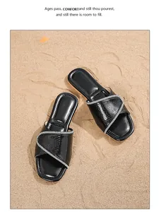 Primer plano de sandalias bohemias negras de punta cuadrada con pedrería en arena