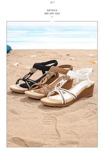 Gros plan de sandales compensées bohèmes avec boucles florales sur une plage ensoleillée