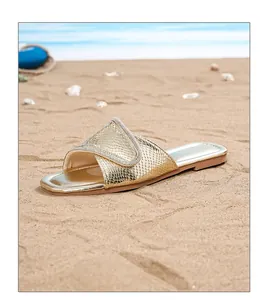 Detalle de sandalias planas bohemias doradas con pedrería sobre la arena de una playa
