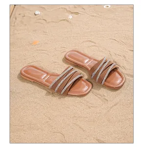 Nahaufnahme der flachen Bohemian-Sandalen mit Strassriemen auf weichem Sand am Strand